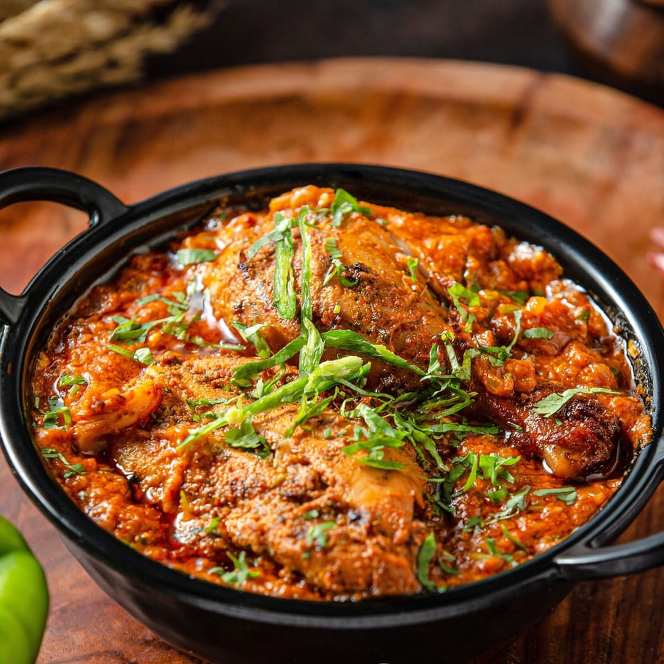 Indian chicken curry in a black bowl, garnished with fresh green herbs.