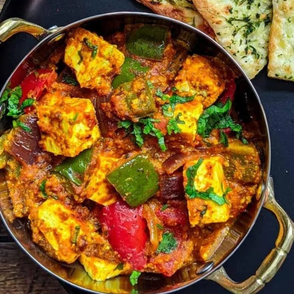 A close-up of Indian paneer curry with bell peppers and cilantro, served with naan bread.