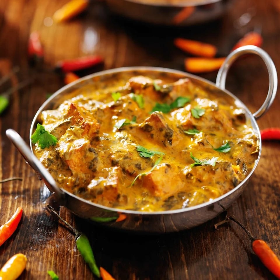 Indian curry with chicken and spinach in a metal bowl on a wooden table with chilies.